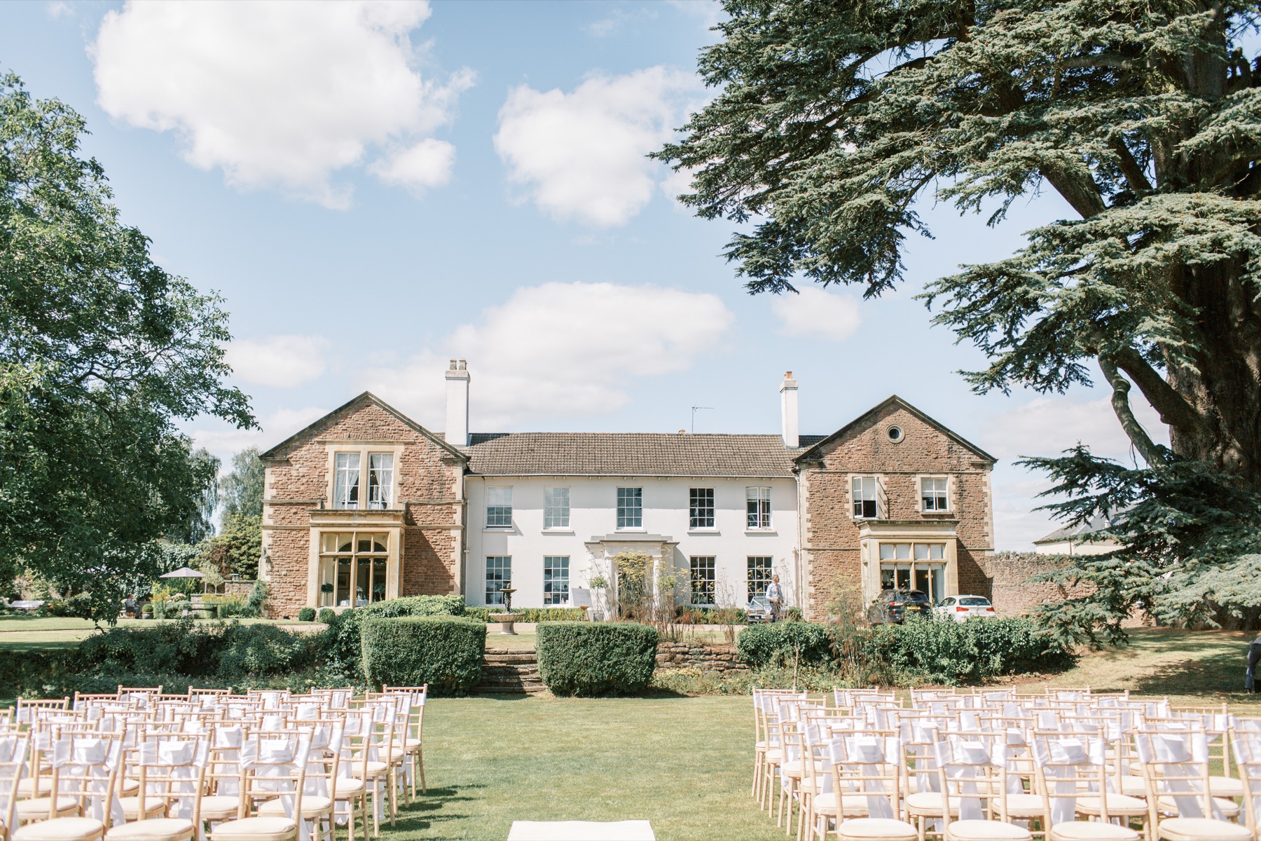 The Glewstone Court manor house with ceremony chairs set by the driveway beneath the cedar